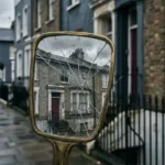 Cracked handheld mirror reflecting a weathered Victorian terraced house on an overcast London street, distorting its true value.